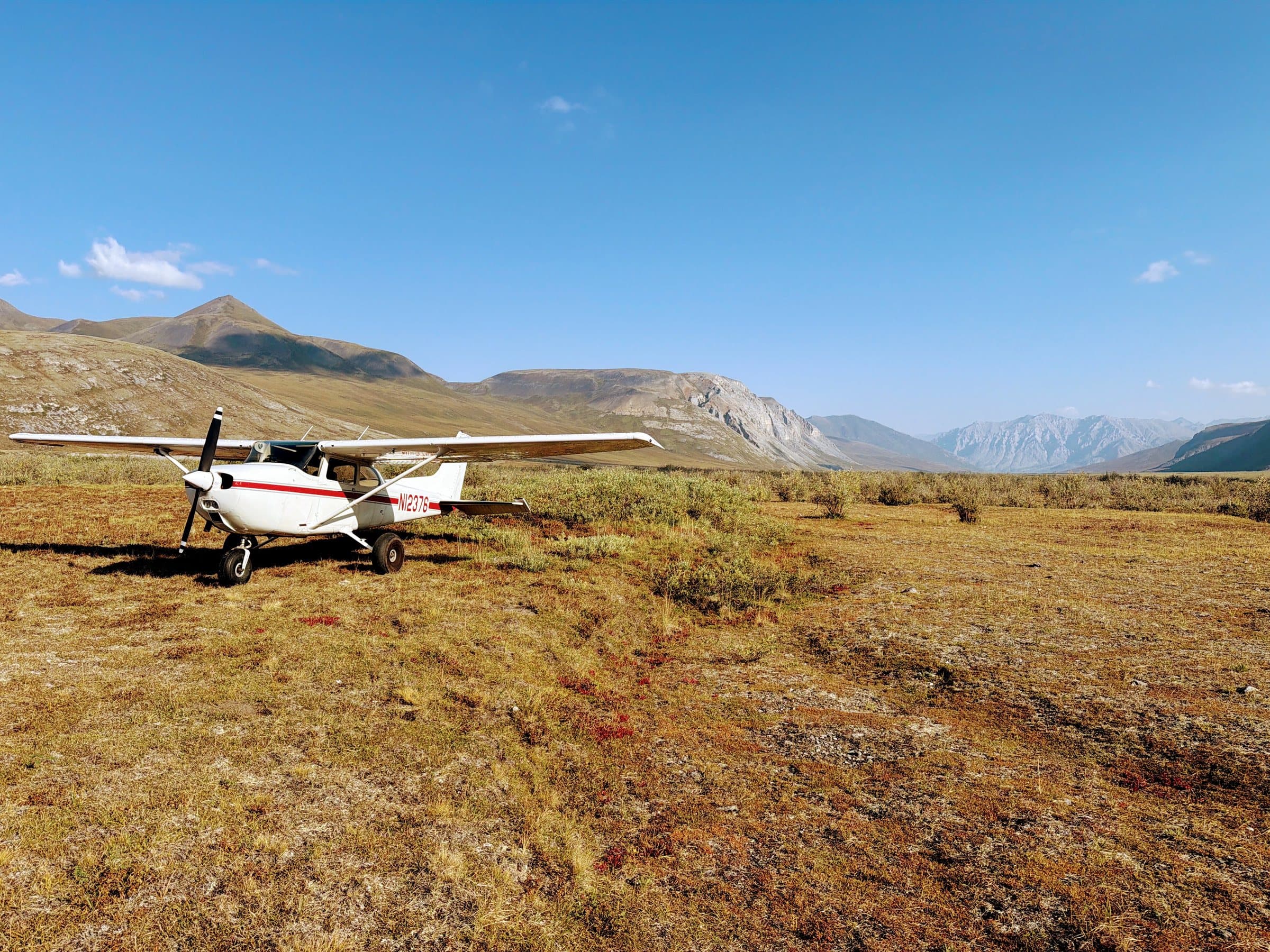 White bush plane on a dirt airstrip in an Alaskan tundra valley, ochre hills under a steel-blue sky.